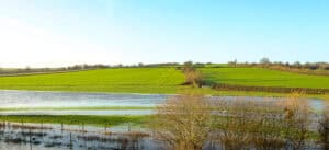 Flooded low-lying fields beside dry higher farmland, showing why building on floodplains is tightly controlled.