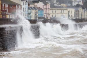 Storm waves overtopping a coastal sea wall by seafront houses, the kind of tidal flood risk that climate change allowances assess.
