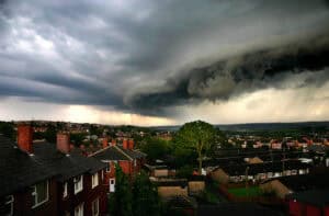 A dark shelf cloud and bands of rain sweeping over a UK town, the kind of sky a weather bomb brings.