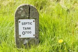 Concrete marker post labelled septic tank on a grass verge, marking a private system subject to septic tank regulations.