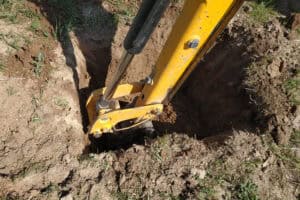 Mini-excavator digging a soakaway trial pit in soil for BRE365 infiltration testing on a development site.