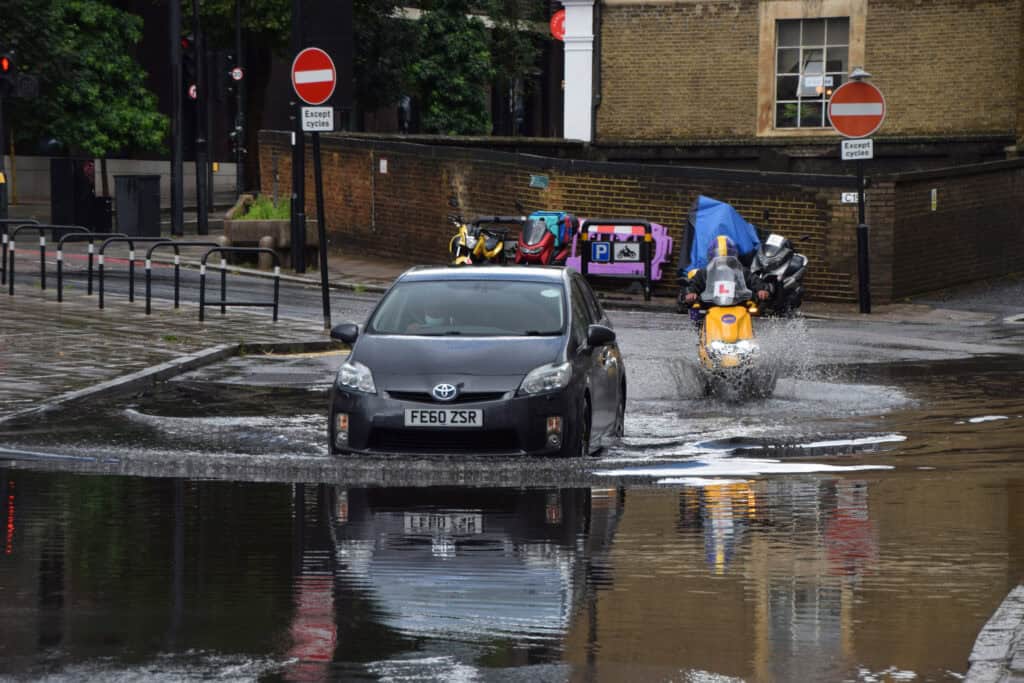 London, UK - August 7 2021: A car splashes through a flooded Farringdon Lane in central London after a day of heavy rain.