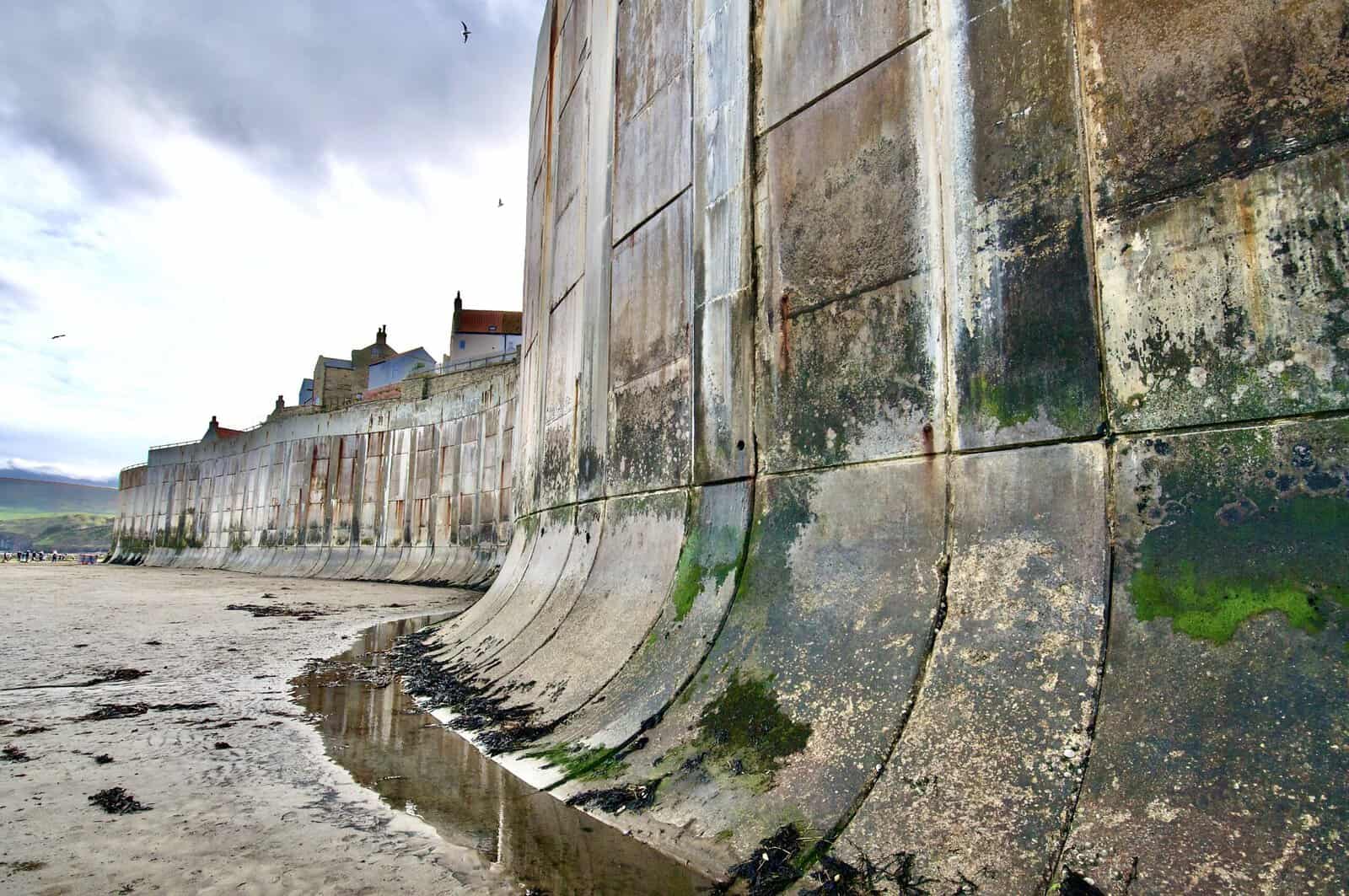 Recurved concrete sea wall at low tide, one of the hard coastal flood defences, shaped to turn waves back out to sea.