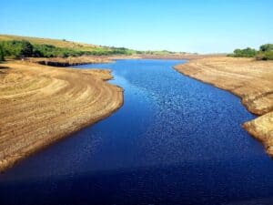 Severely depleted UK reservoir with wide exposed banks during drought, the parched conditions behind the floods in a drought paradox.