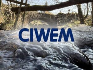 CIWEM logo over a fast-flowing stream beneath a stone arch bridge, for an article on the Chartered Institution of Water and Environmental Management.