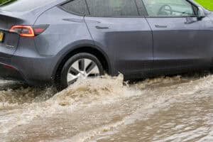 Electric car driving through deep muddy flood water, showing how to drive through flood water safely.