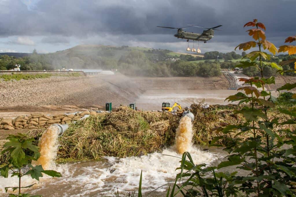 Military helicopter and pumps during repair work at Toddbrook Reservoir, an ageing water infrastructure failure of the same kind as a canal breach.