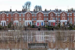 Does flood risk affect house prices: floodwater covers a riverside park in front of a terrace of period brick houses.