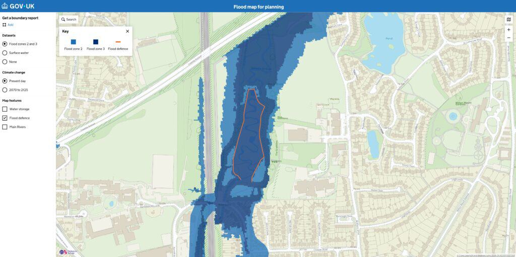 Environment Agency Flood Map for Planning showing flood defences marked in orange running alongside the watercourse, with the surrounding flood zone still shaded