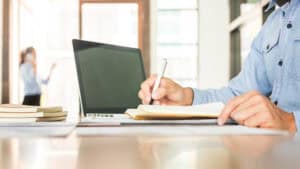 Consultant making notes beside a laptop while working through how to do a flood risk assessment for planning.