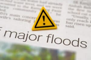Warning sign on a newspaper headline about major floods, illustrating why a conveyancing flood report is not enough for planning.