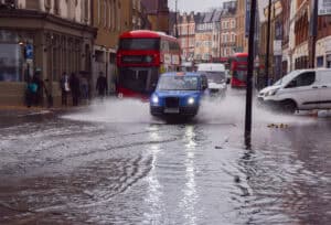 Surface water flooding in a London street with vehicles driving through standing water after heavy rainfall