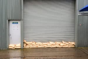 Sandbags lined along a commercial roller-shutter door and fire exit to hold back floodwater, a temporary flood-resistance measure.