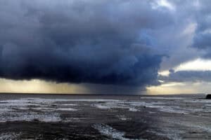 Heavy rain falling from storm clouds over a rough UK coast, illustrating the climate whiplash between flood and drought.