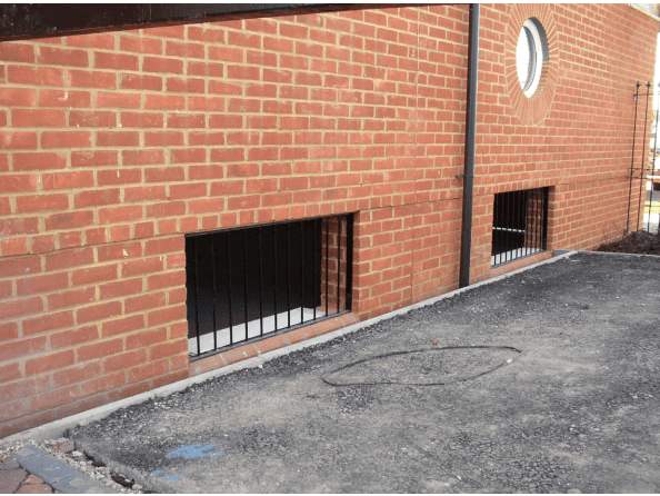 Floodable void grilled openings at the base of a brick undercroft, letting floodwater pass while keeping debris out.