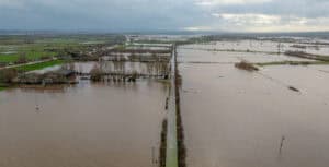 Aerial view of Somerset Levels flooding, with brown floodwater across farmland either side of a raised road.