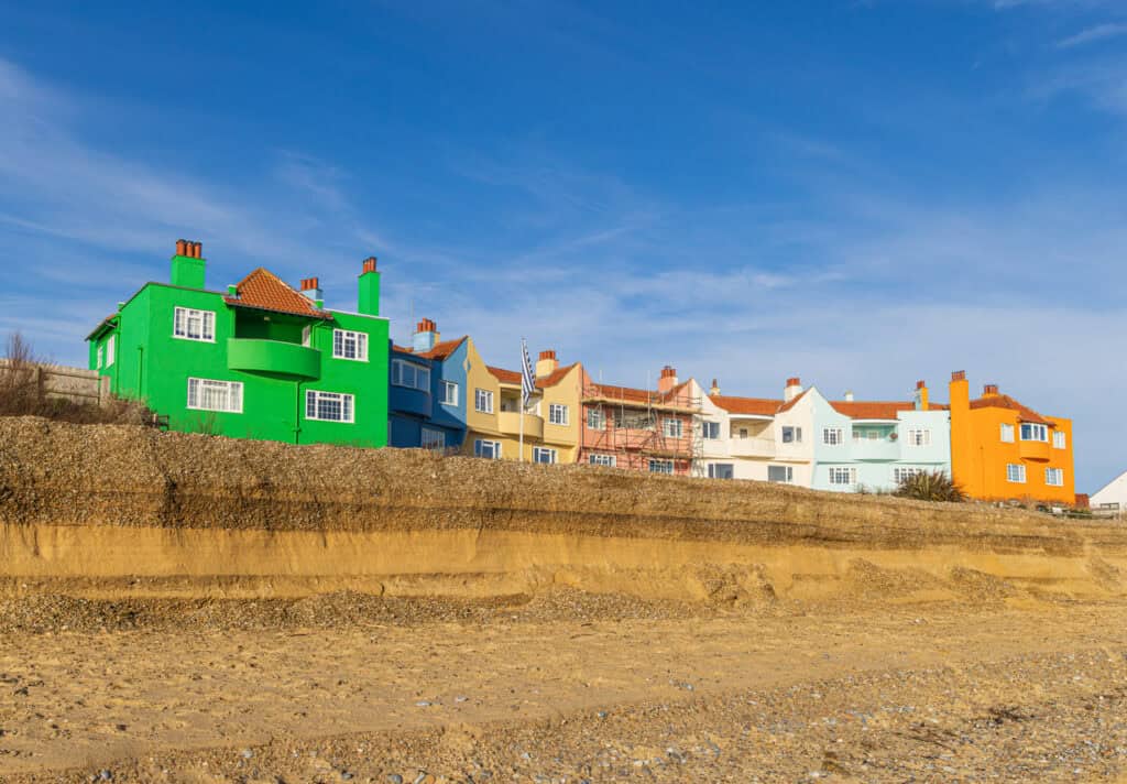Colourful seafront houses above an eroded cliff edge, the sharp end of the coastal erosion compensation UK debate.