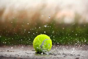 Tennis ball splashing on a rain-soaked court, illustrating why grass court drainage decides when play can continue.