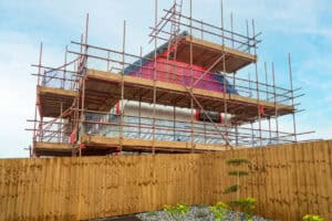 Part-built house clad in scaffolding behind a new timber fence, illustrating a retrospective planning application.