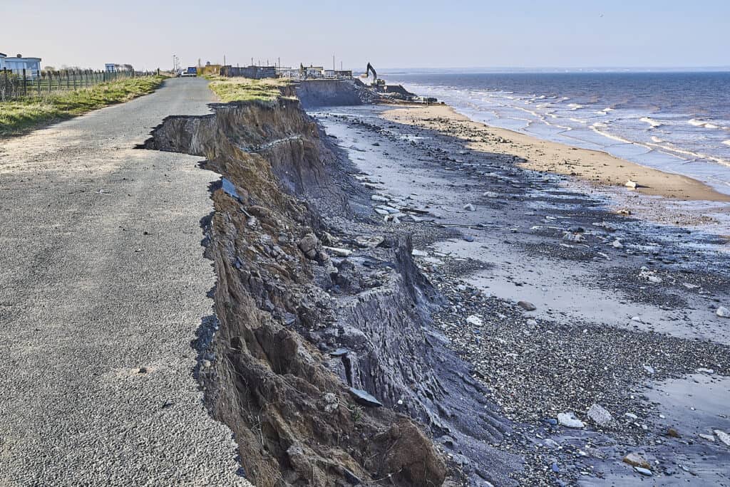 Collapsed clifftop road ending at an eroding coastline, the kind of loss that sea level rise planning must anticipate beyond 2100.