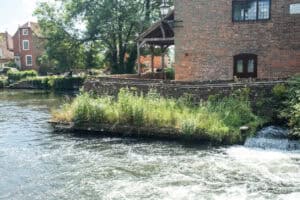 A weir and riverside building on a chalk stream, the kind of watercourse managed under the Romsey flood alleviation scheme.