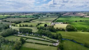Aerial view of a campsite on low-lying farmland beside a watercourse, the setting a campsite flood risk assessment must address.