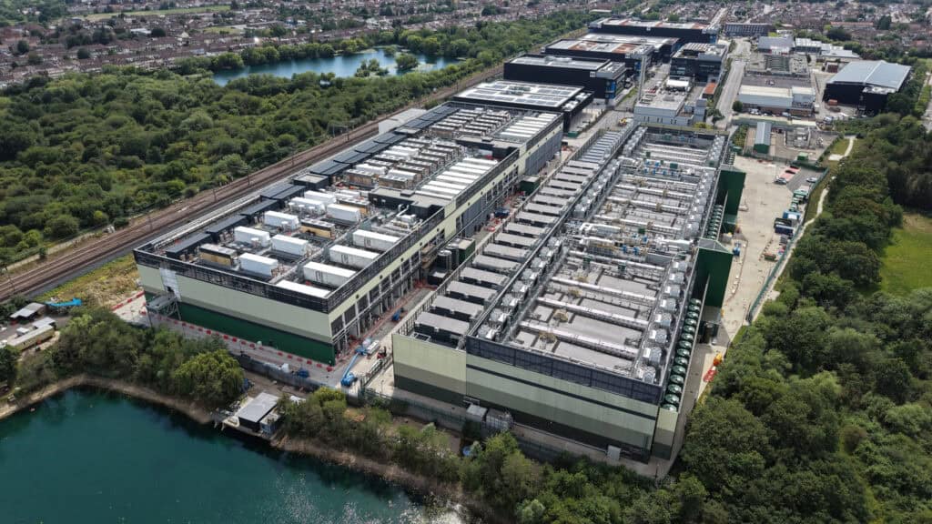 Large data centre campus with plant-covered roofs beside open water, the setting a data centre flood risk assessment has to address.