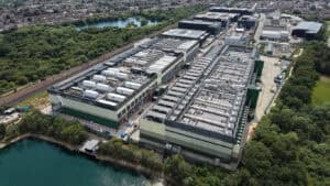 Large data centre campus with plant-covered roofs beside open water, the setting a data centre flood risk assessment has to address.