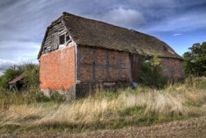 Derelict timber-framed and brick barn in an overgrown field, the kind of rural building a flood risk assessment for a barn conversion covers.