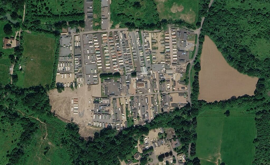 Aerial view of a caravan and mobile home site beside a large body of silt-laden brown water, illustrating gypsy and traveller site flood risk assessment.
