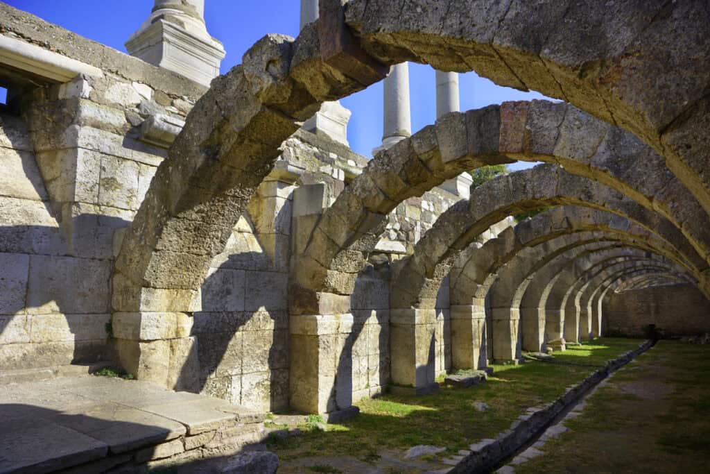 Rows of Roman stone arches beside a stone-lined channel, evoking the Roman drainage system and water engineering.