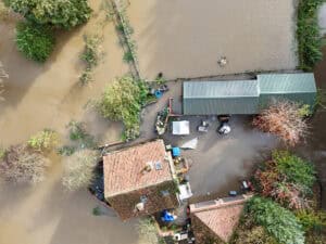 Aerial view of floodwater around a rural house and outbuildings, the kind of event a section 19 flood investigation records.