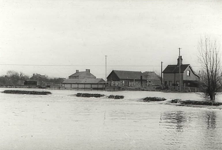 Water spilling over a sandbag line in front of fen buildings during the 1947 floods near Earith.