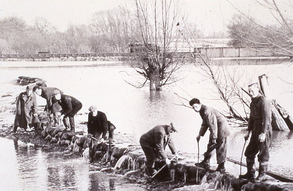Men working a sandbag line as water overtops it during the 1947 floods in the fens near Earith.