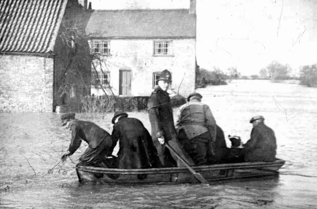 A boat worked through floodwater past a cottage during the 1947 floods at Laneham, a police constable aboard.