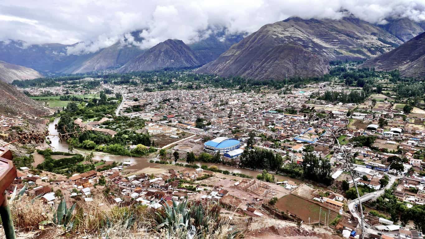 An Andean valley town spread across the floodplain, with the river running high and brown with sediment after rain.