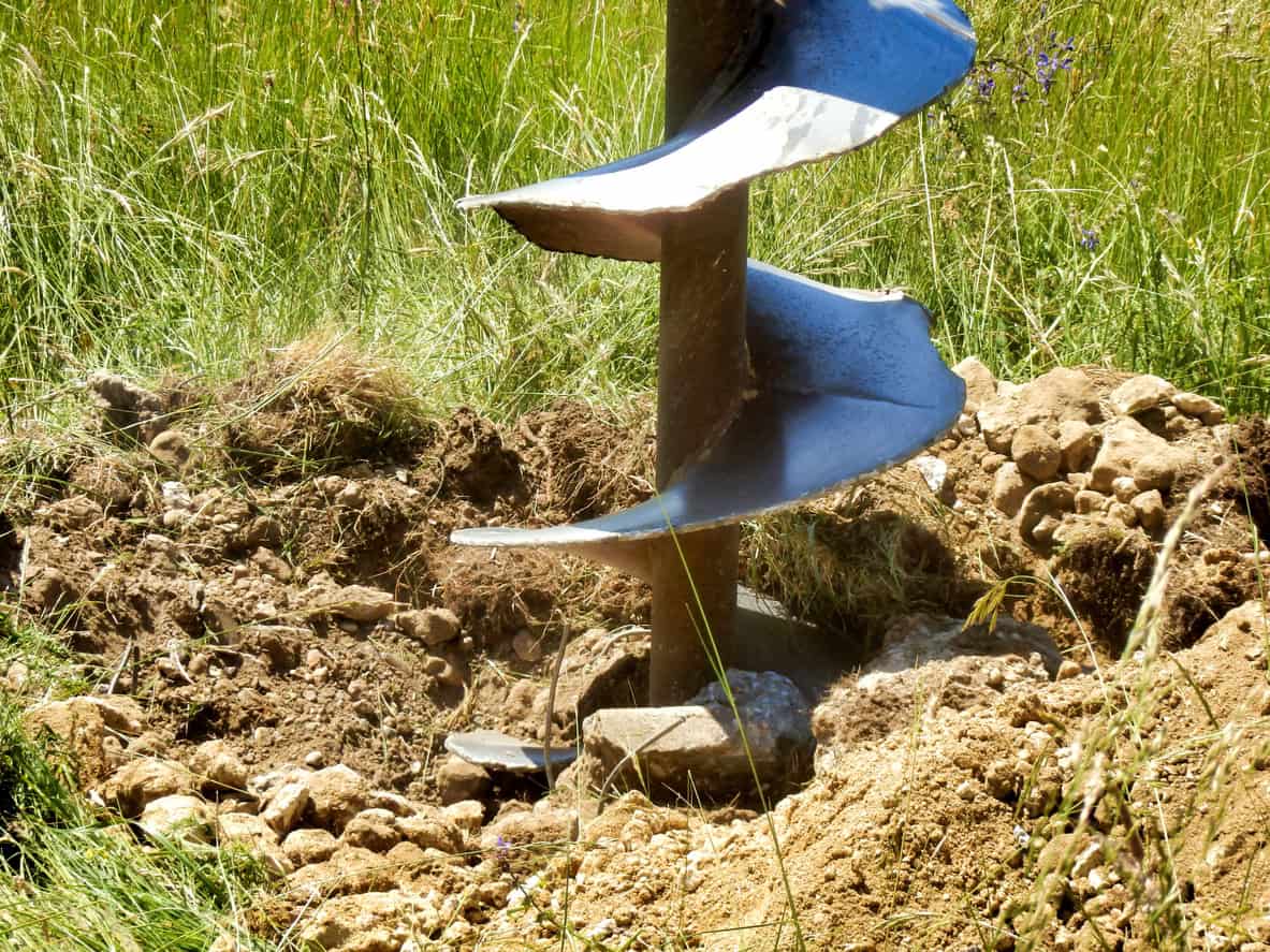 Helical auger boring into chalky, stony ground during a ground investigation, with spoil around the hole.