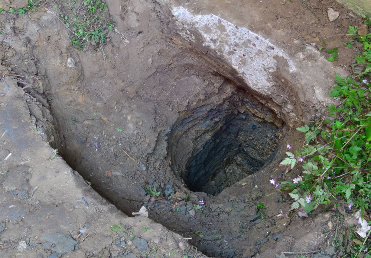 Hand-dug excavation exposing soil over layered rock, the kind of ground profile British Geological Survey borehole records describe.