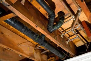Black plastic soil and waste pipework running between timber floor joists, the sanitary pipework BS EN 12056 covers.