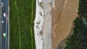 Aerial view of hard coastal flood defences: a concrete sea wall and promenade along the foot of a chalk cliff below a coast road.