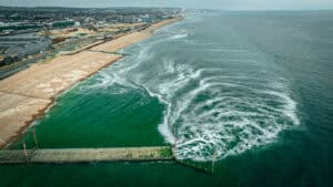 Aerial view of foam and discoloured water in the surf beside coastal groynes, the coastal setting where dry weather flow limits apply.