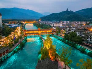 Water diverted by the Dujiangyan irrigation system running through the town at dusk, split around a mid-river island.