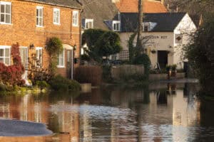 Floodwater standing across a village lane beside brick cottages and a pub, the kind of ground Flood Zone 3b covers.