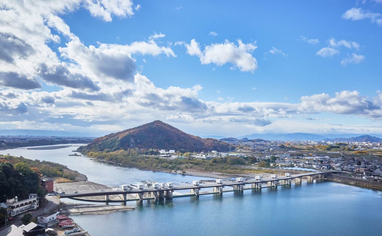 Large Japanese river passing a gated barrage as it leaves the hills for a populated plain, the setting an open levee was built for.
