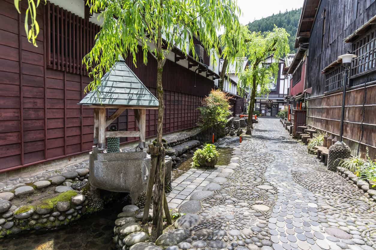 Open water channel running beside a stone-paved lane in a traditional Japanese town, with a covered washing basin.