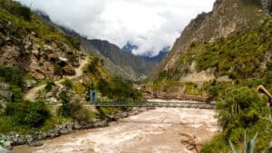 A steel footbridge over a river in spate, in the kind of steep catchment that Machu Picchu drainage discharges to.