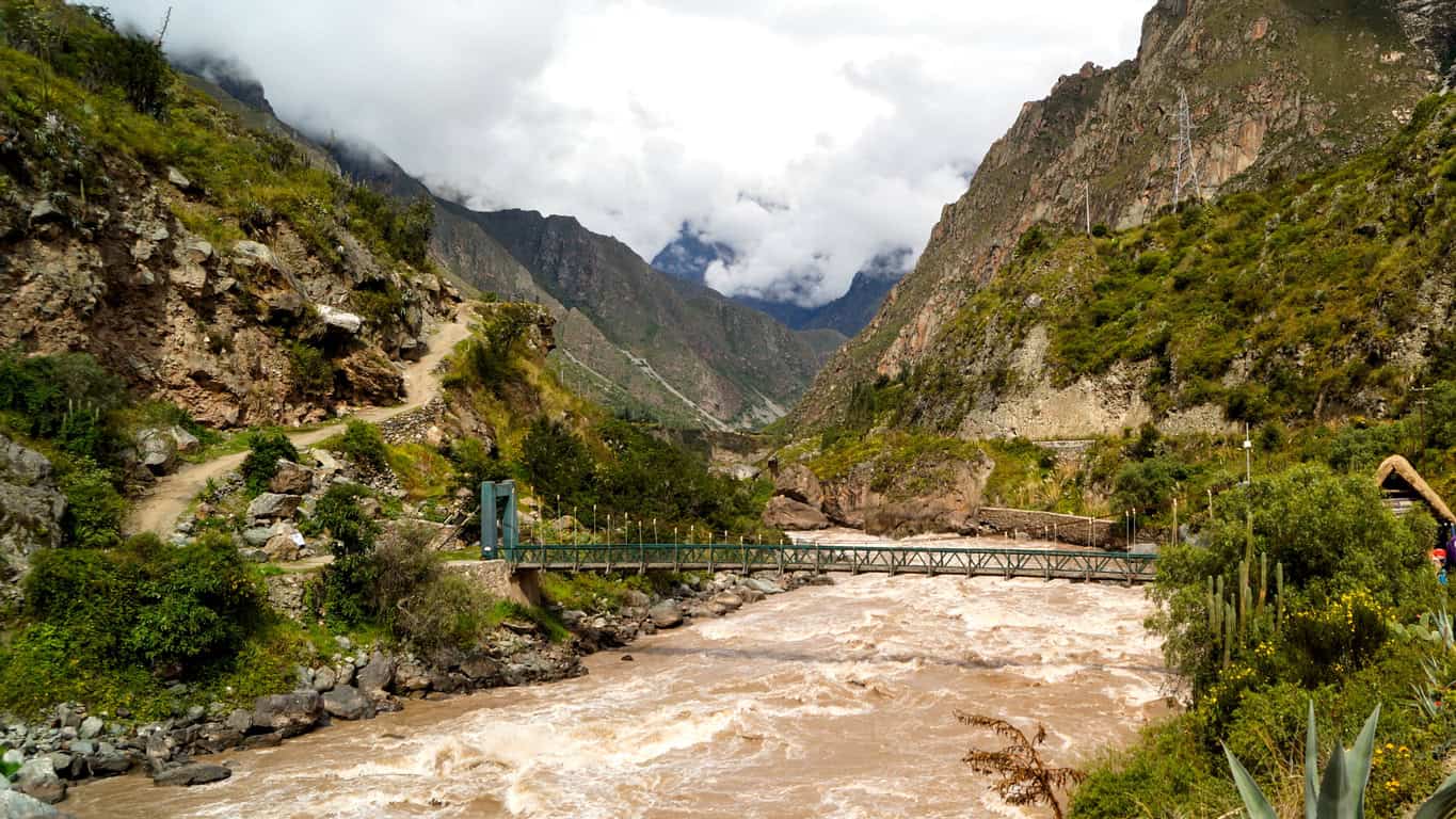 A steel footbridge over a river in spate, in the steep catchment that receives runoff from the surrounding slopes.