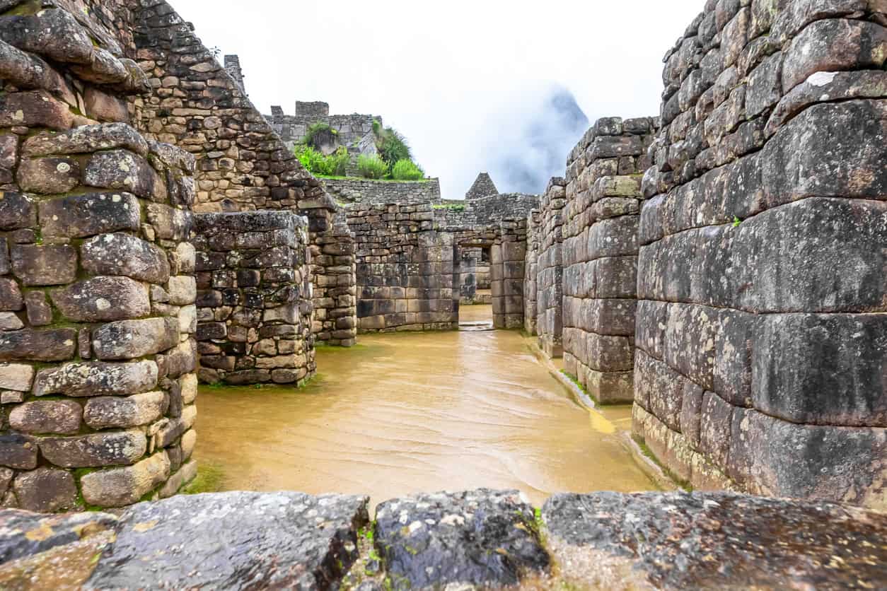 Rainwater crossing the floor of a stone enclosure, showing Machu Picchu drainage in the wet conditions it was built for.