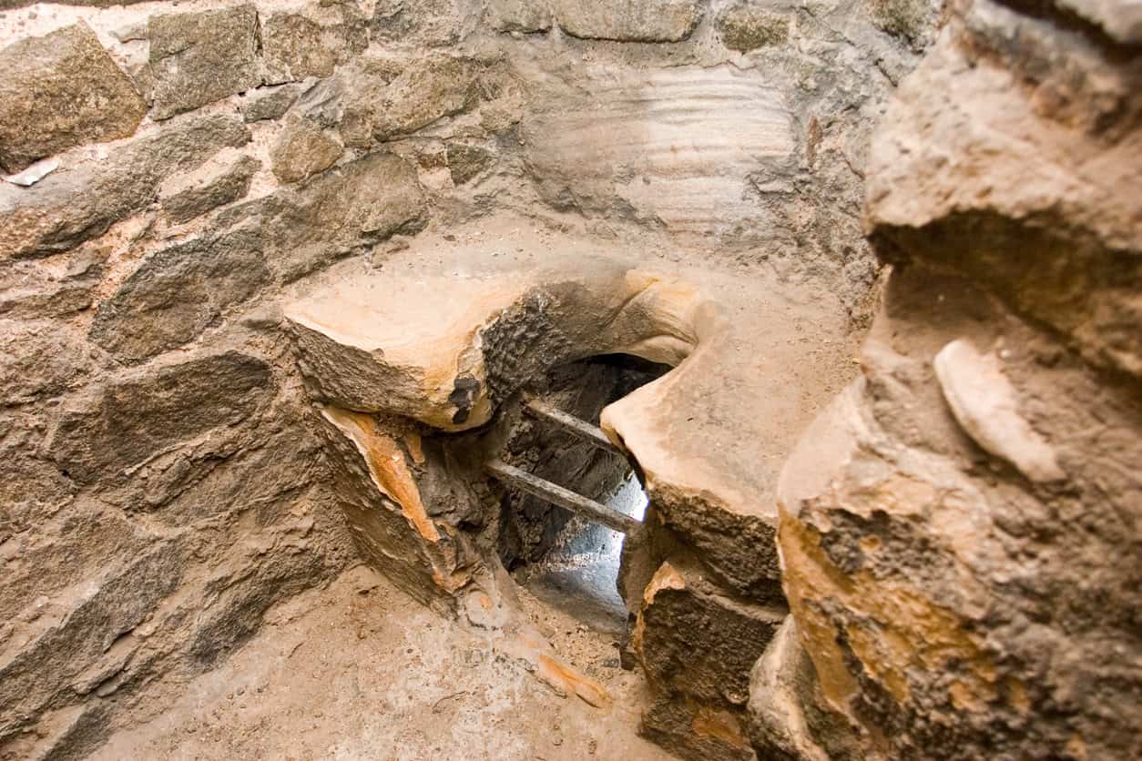 Stone garderobe seat and shaft in a castle wall, the domestic end of medieval drainage, now closed with a metal grille.