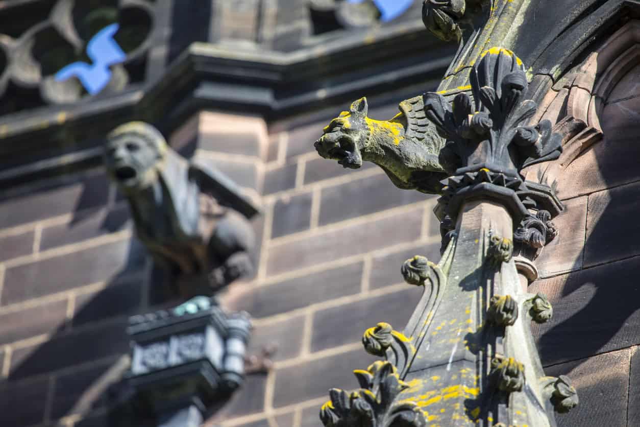 Carved gargoyle waterspouts projecting from a sandstone church pinnacle, the roof-water end of medieval drainage.